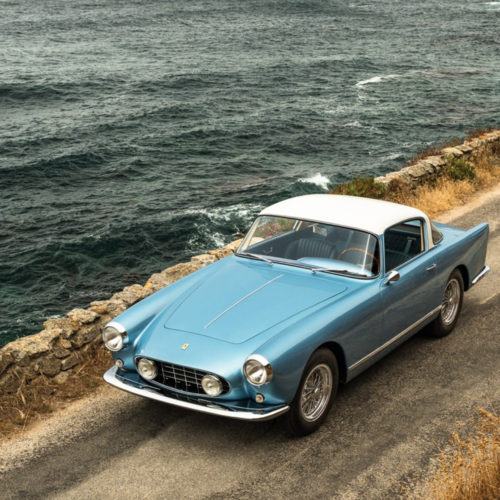 Blue classic Ferrari coupe driving along a coastal road