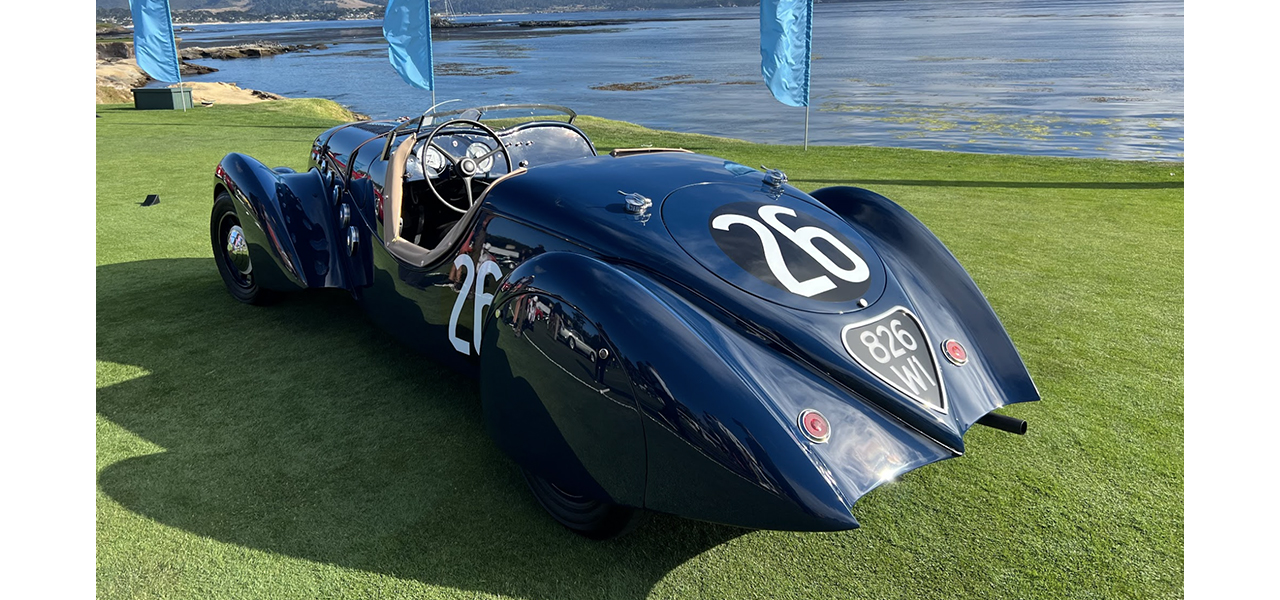 Dark blue vintage racing automobile displayed on a coastal concours lawn